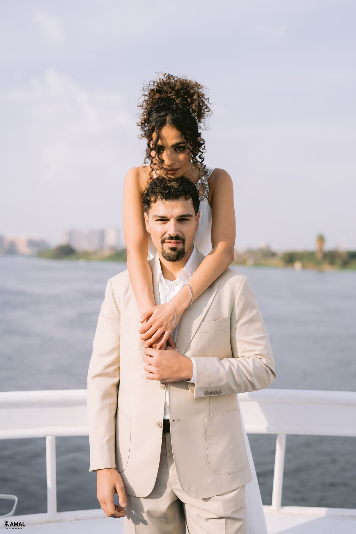 Salma with her arms around Anas's shoulders, the river behind them